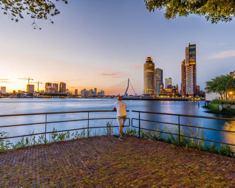 Iemand kijkt uit over de Maas naar de skyline bij zonsondergang